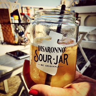 Hand holding Disaronno Sour Jar cocktail on sunny patio