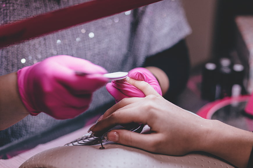 Close-up of pink gloves applying nail polish in salon