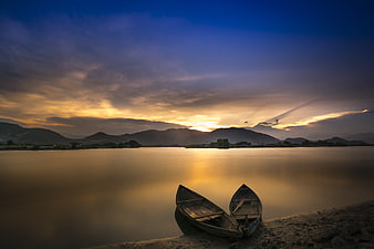Two wooden boats on riverbank at sunset with mountains