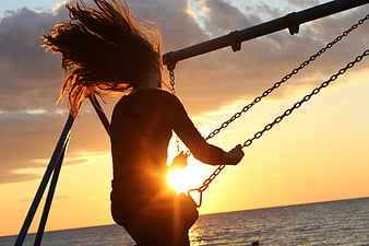 Silhouette of Girl Swinging at Sunset by the Sea