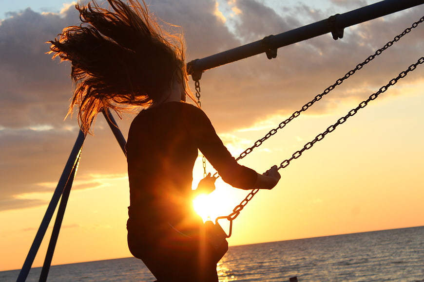 Silhouette of Girl Swinging at Sunset by the Sea