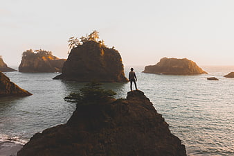 Man Standing on Rocky Cliff Overlooking Ocean at Sunset
