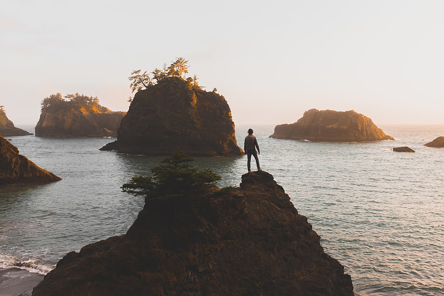 Man Standing on Rocky Cliff Overlooking Ocean at Sunset