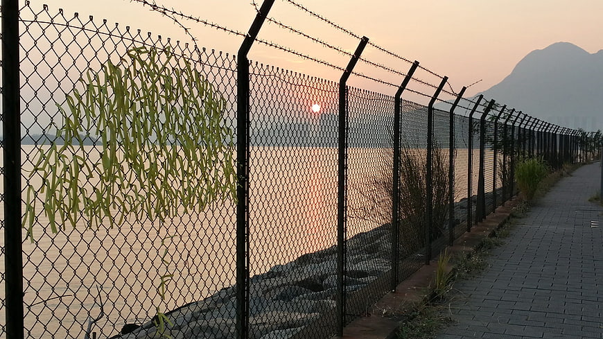 Chain link fence with barbed wire along waterfront at sunset