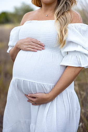 Pregnant woman in white dress holding belly outdoors