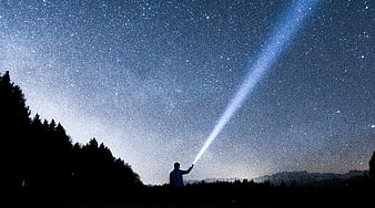 Man pointing flashlight beam into starry night sky