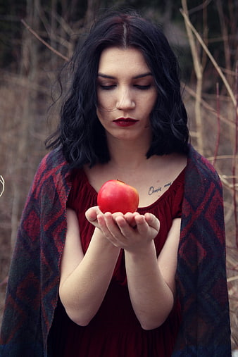 Woman holding red apple in forest with dark hair
