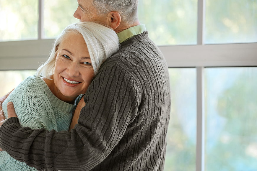 Happy Senior Couple Hugging Indoors by Window