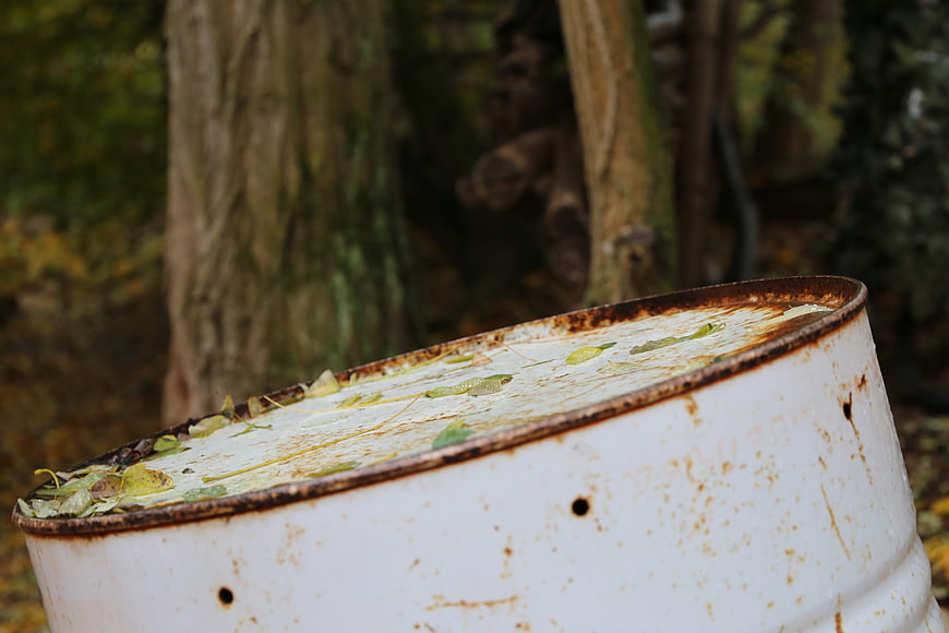 Rusty white metal barrel in autumn forest