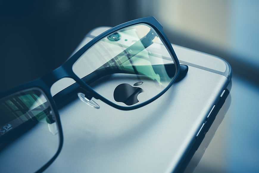 Black Glasses Resting on Silver Smartphone with Apple Logo