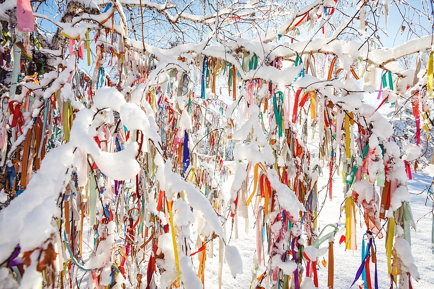 Colorful ribbons hanging on snow-covered tree branches in winter