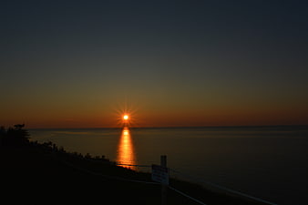 Sunset over calm ocean with starburst effect and silhouette