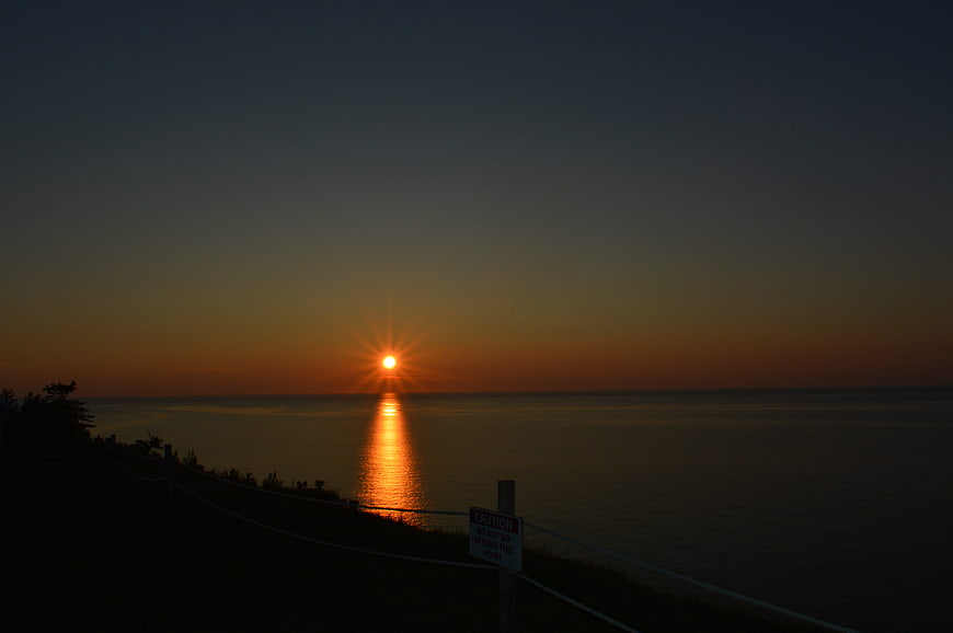 Sunset over calm ocean with starburst effect and silhouette