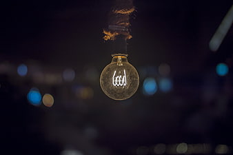 Glowing vintage incandescent light bulb hanging against dark bokeh background