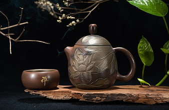 Carved Clay Teapot and Cup on Wooden Plank with Green Leaves