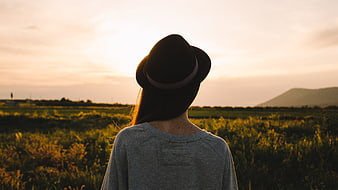 Woman in Hat Looking at Sunset Over Green Field