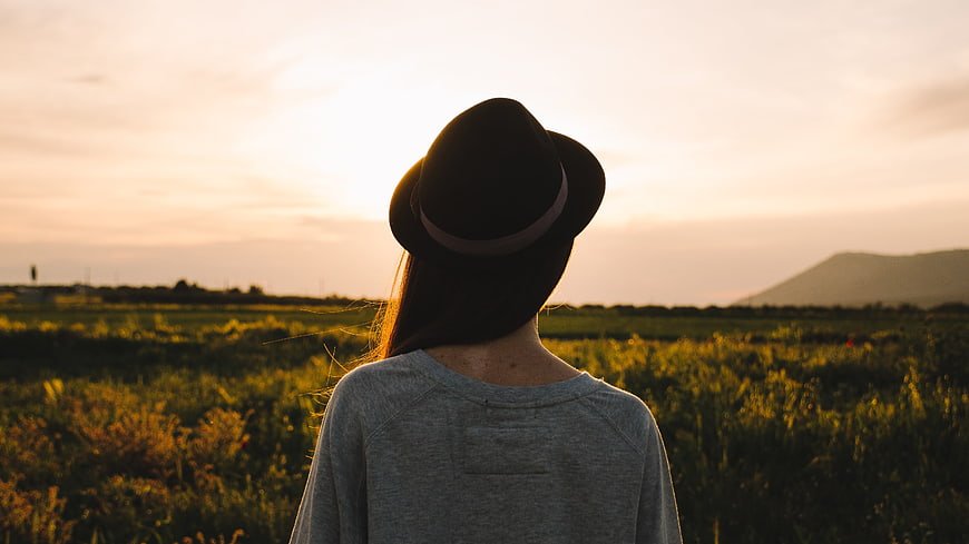 Woman in Hat Looking at Sunset Over Green Field