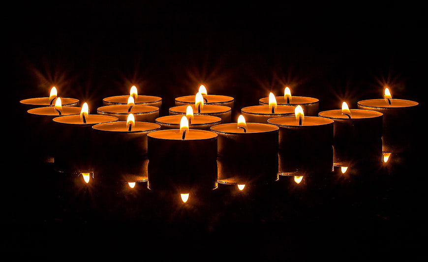 Rows of lit tea light candles with reflections on dark background