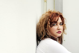 Portrait of woman with curly red hair against white wall