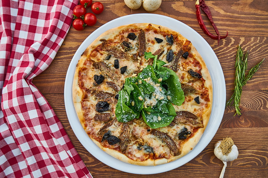 Flat lay of gourmet pizza with anchovies and spinach on wooden table