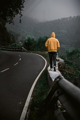 Man in yellow jacket walking on misty mountain road