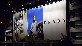 Large Prada fashion billboard advertisement on urban building at night
