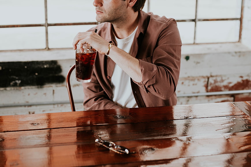 Man drinking iced soda at rustic wooden cafe table