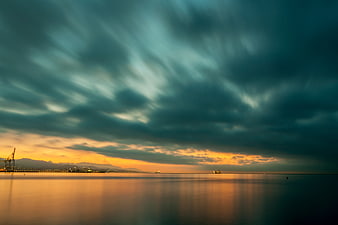 Dramatic Sunset Over Calm Sea with Port Cranes and Mountains