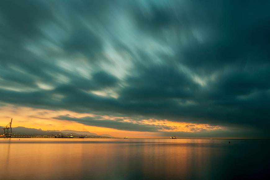 Dramatic Sunset Over Calm Sea with Port Cranes and Mountains