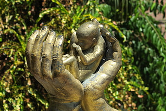 Bronze Statue of Hands Protecting a Fetus Against Green Foliage