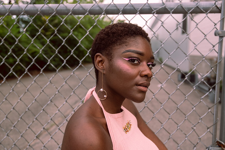Stylish Black Woman with Pink Makeup by Chainlink Fence