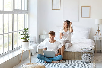 Young couple relaxing in bright bedroom with laptop and coffee