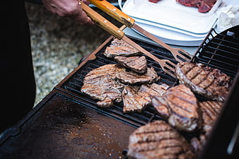 Close-up of beef steaks grilling on barbecue with tongs