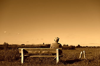 Elderly man sitting on a wooden bench in a field