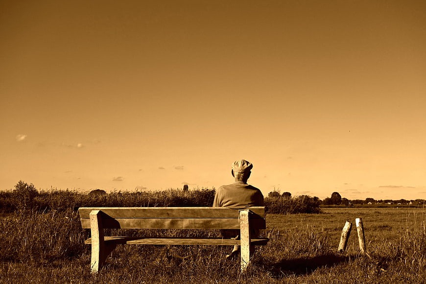 Elderly man sitting on a wooden bench in a field