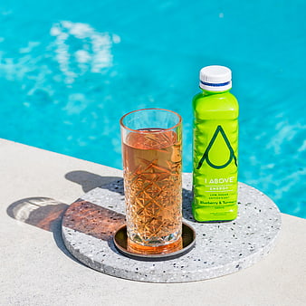 Green energy drink bottle and glass by poolside