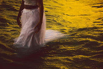 Woman in white dress standing in golden ocean waves