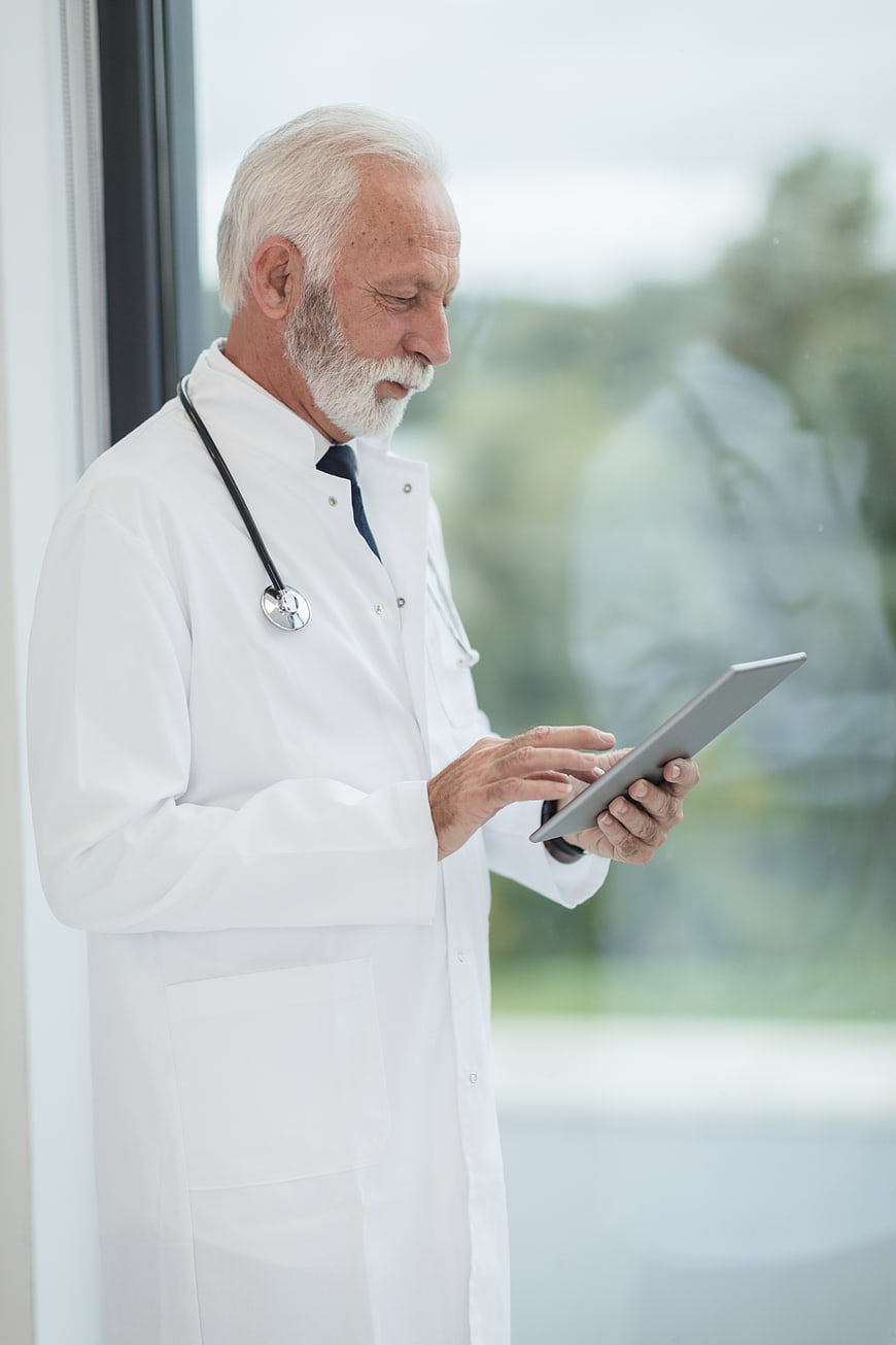 Senior Doctor Using Tablet by Window