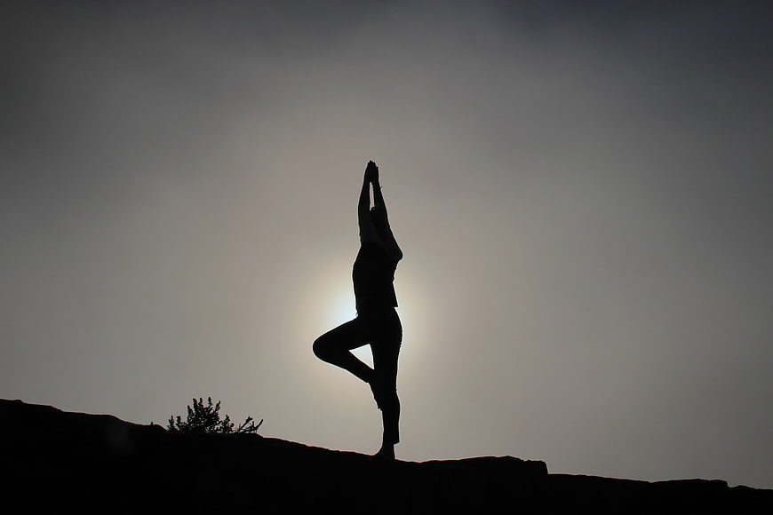Silhouette of woman doing yoga tree pose at sunset