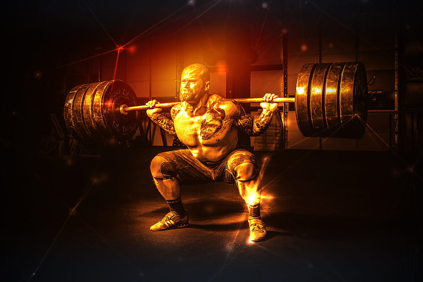Muscular man performing a heavy barbell squat in a dark gym