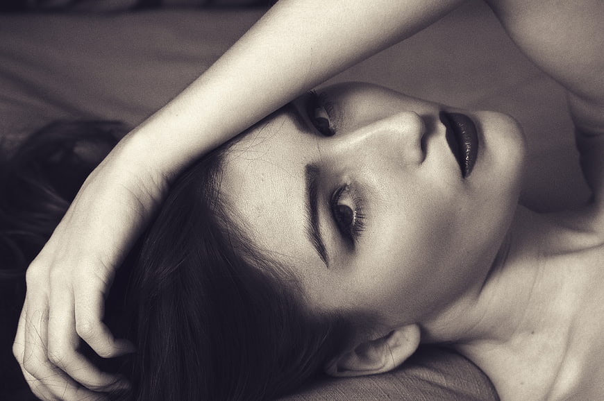 Black and white portrait of a woman lying down with arm over face