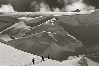 Three skiers ascending a snowy mountain slope in black and white