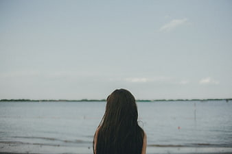 Woman with long hair looking out at the ocean horizon