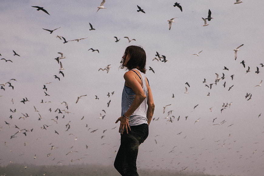 Woman standing amidst flock of flying seagulls