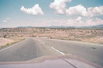 Vintage POV shot of a desert highway with blue sky and clouds