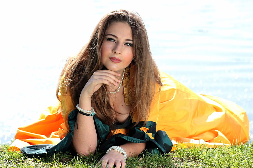 Young woman in yellow dress lying on grass by a lake