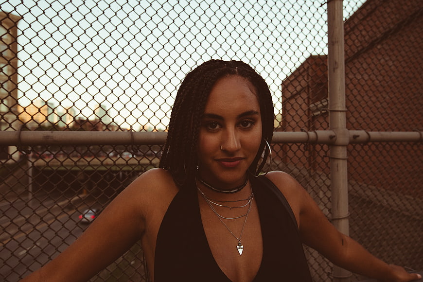 Stylish Woman with Braids Leaning on Chainlink Fence