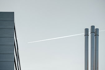 Minimalist industrial architecture with smokestacks and contrail