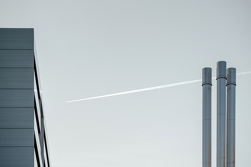 Minimalist industrial architecture with smokestacks and contrail