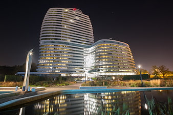 Modern curved office building illuminated at night with reflection